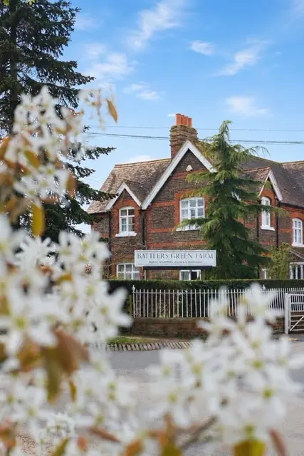 Traditional brick farmhouse with a sign for Battlers Green Farm under a blue sky and white flowering branches in foreground