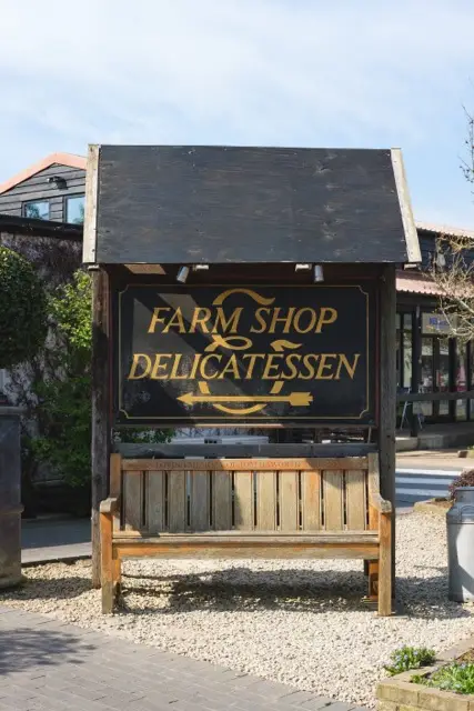 Wooden sign for farm shop and delicatessen with bench beneath, set in outdoor shopping village