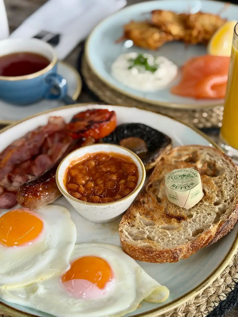 Full English breakfast with eggs, beans, bacon, sausage, tomato, mushroom, toast, tea, and orange juice