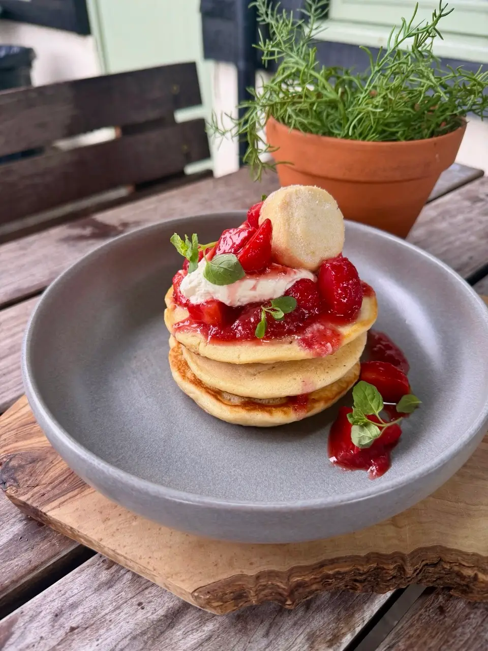Stack of pancakes topped with strawberries, cream, and garnish on a wooden outdoor table