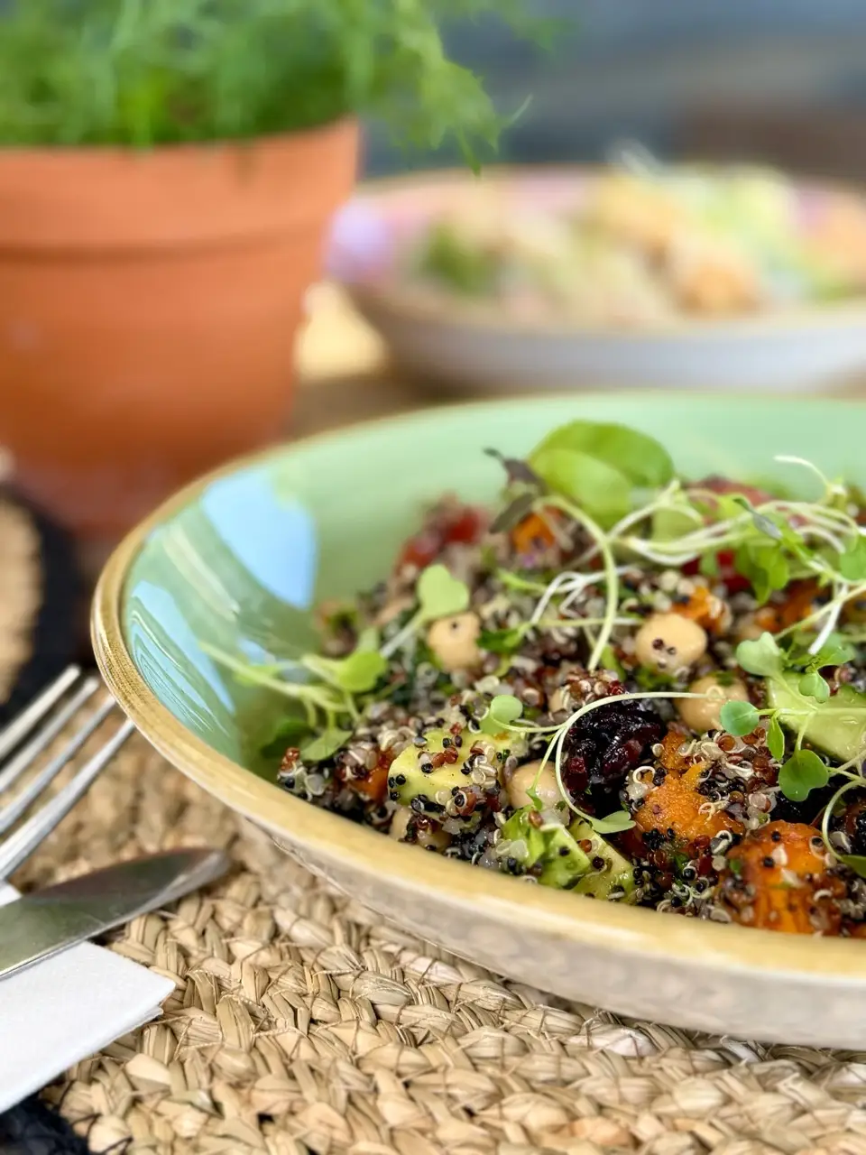 Close-up of quinoa salad with chickpeas, microgreens, and roasted vegetables in a green rimmed bowl