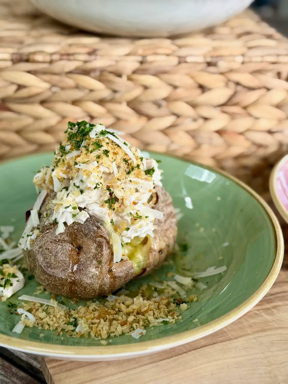 Baked potato topped with creamy filling, grated cheese, herbs, and breadcrumbs on a green plate