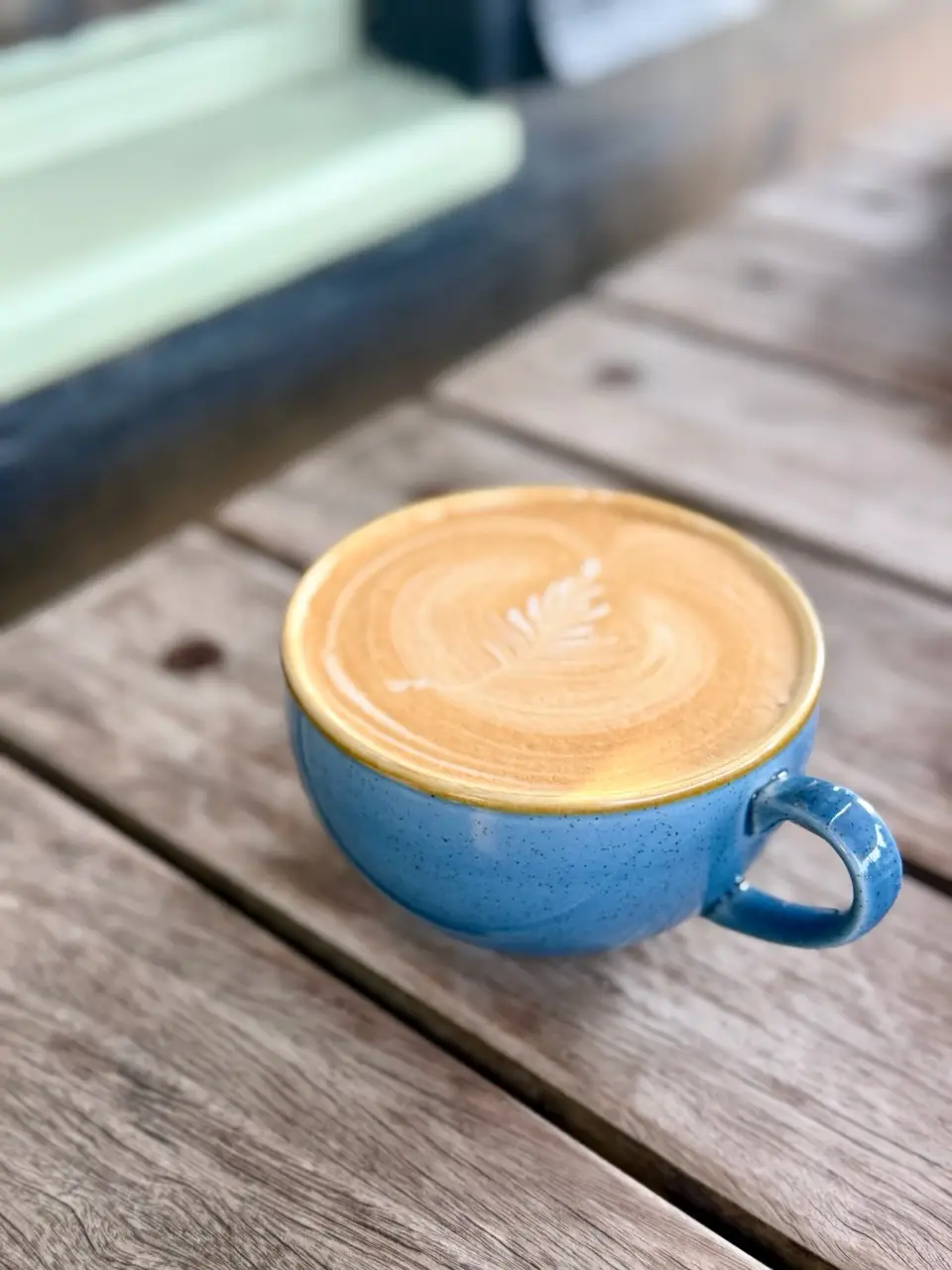 Blue coffee cup with intricate latte art on a wooden table