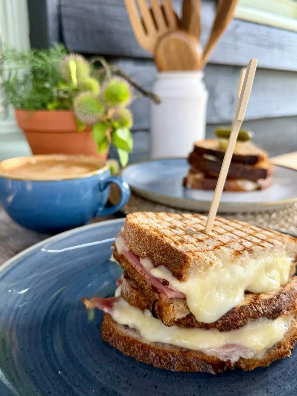 Grilled ham and cheese sandwich with melted cheese and a cup of coffee on blue plates.